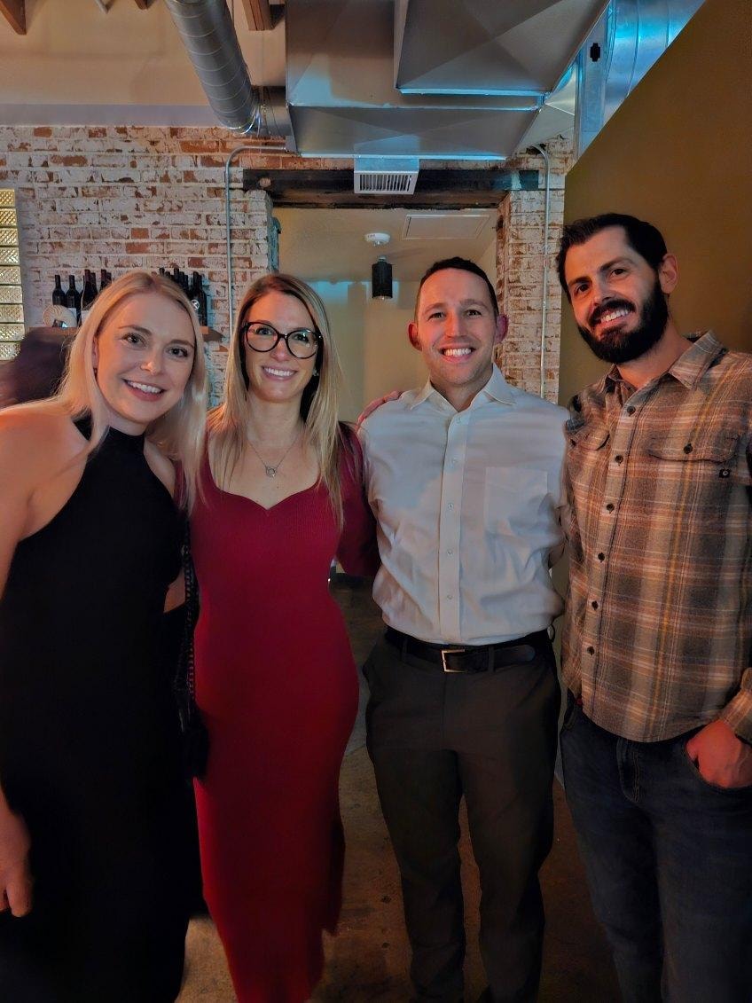 Four people smiling indoors brick wall